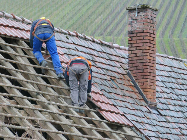 Two men standing on a roof replacing old shingles with new ones